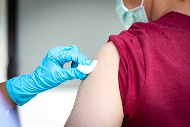 A gloved hand puts cotton wool over the vaccination site on a person's arm.