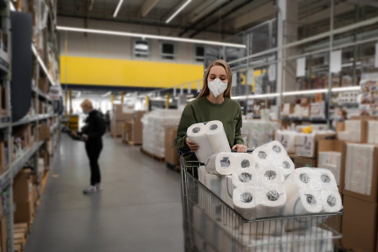 A woman wearing a surgical mask pushing a cart full of toilet paper
