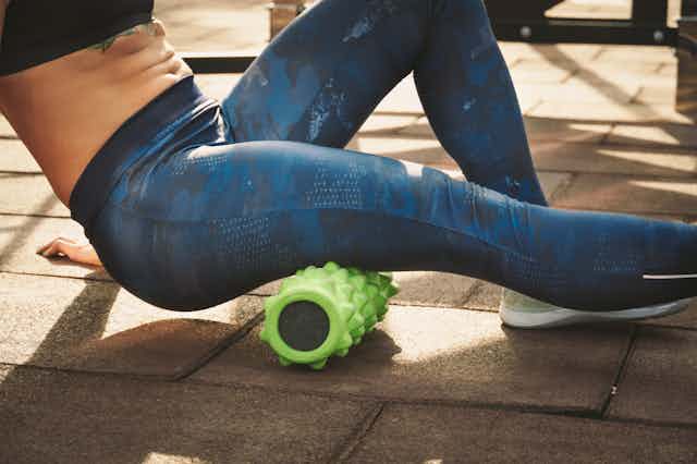 A person wearing exercise clothes and using a foam roller on their leg