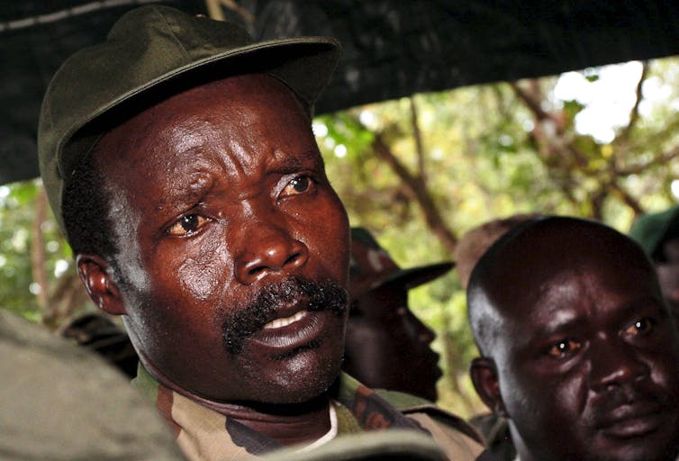 Headshot of Joseph Kony with supporters in tent in jungle