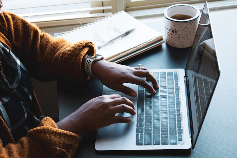 A person types on a laptop with a cup of coffee next to them