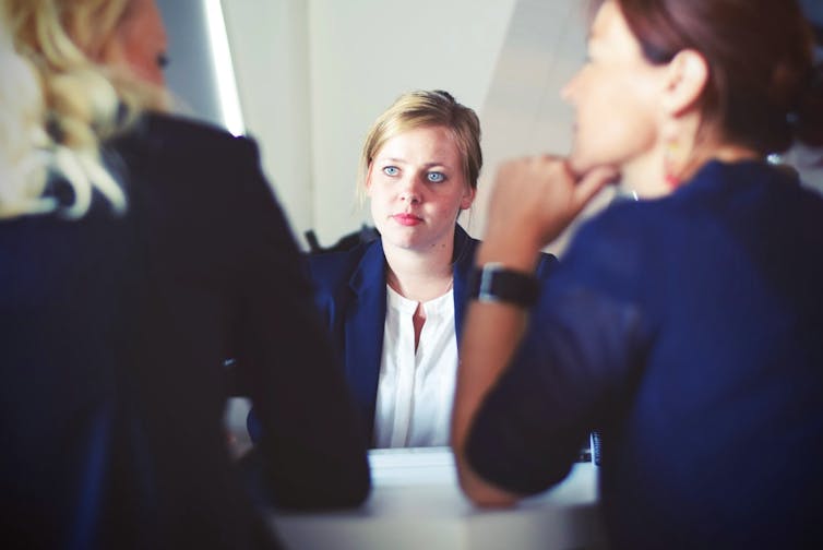 A woman is interviewed by two other women for a job, who are all wearing business suits