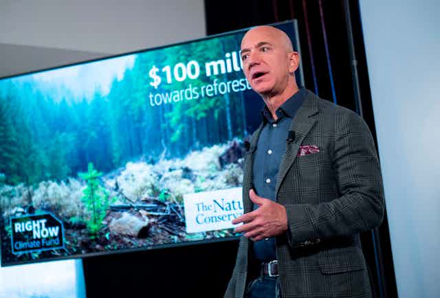Jeff Bezos stands in front of a photo of a forest
