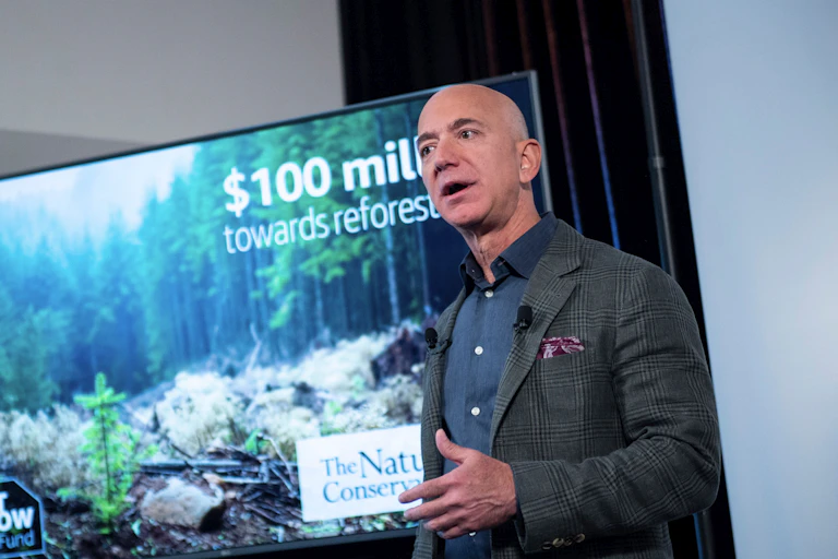 Jeff Bezos stands in front of a photo of a forest