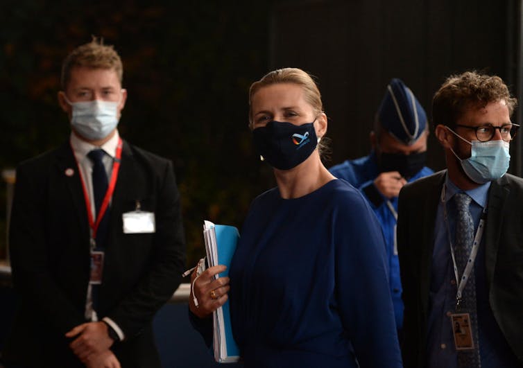 Mette Frederiksen wearing a black mask and holding a folder.