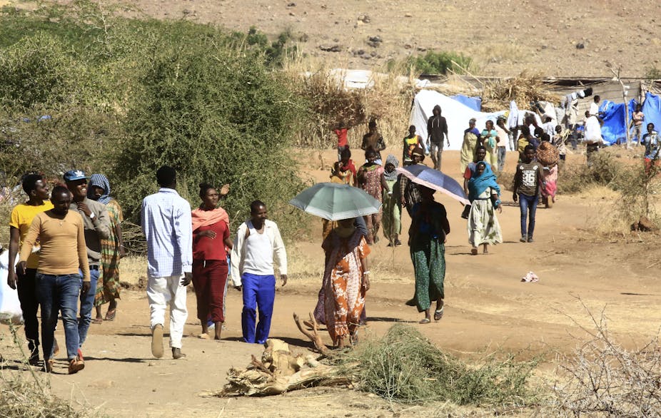 Men and women walking on a path in open country, a tent type of shelter in the background