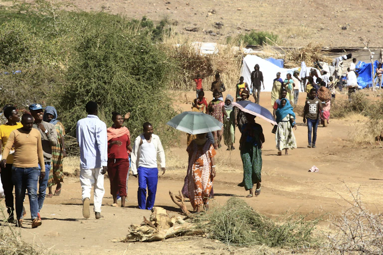 Men and women walking on a path in open country, a tent type of shelter in the background