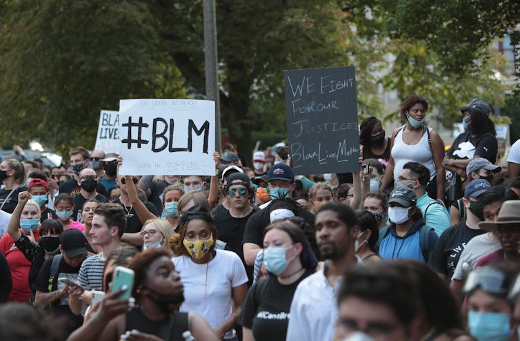 Crowd of mostly Black protesters in face masks hold up BLM and other racial justice signs