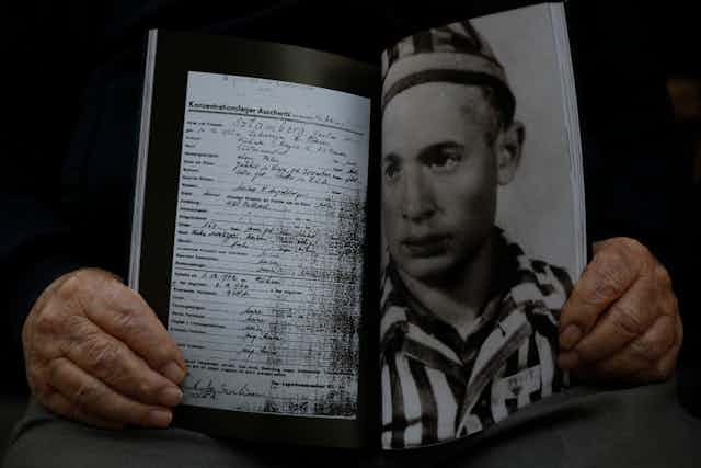 A man holds a photo of himself and his concentration camp record