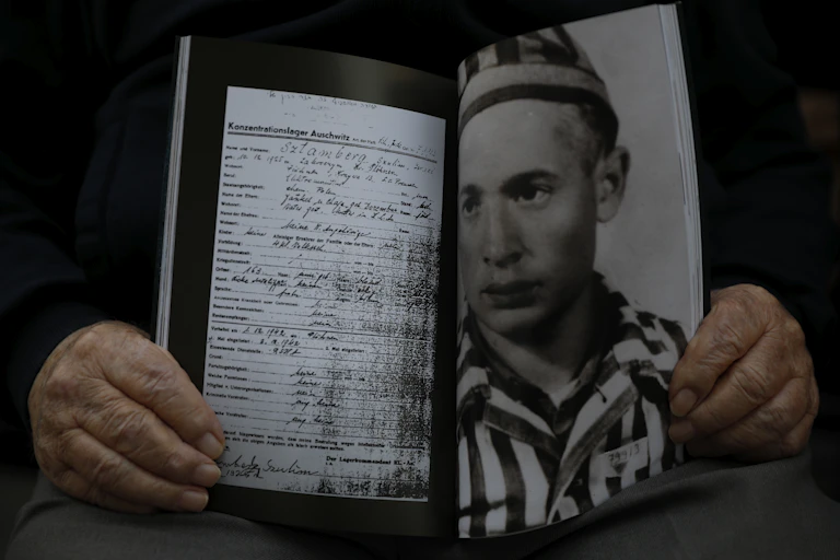 A man holds a photo of himself and his concentration camp record
