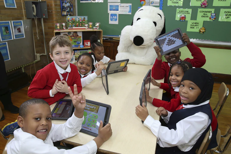 Children sit at a table with devices.