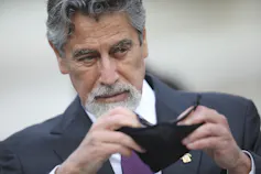 A man with grey beard takes off his face mask.