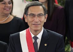 A man with glasses and dark hair smiles.