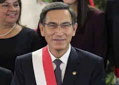 A man with glasses and dark hair smiles.