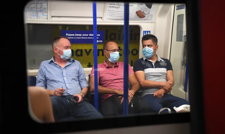 Three men wearing masks on the London underground.