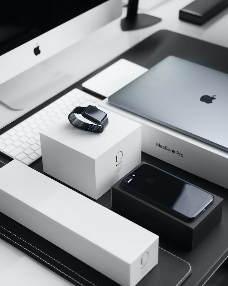 An apple computer, laptop, watch and phone sit on their boxes in a neat order
