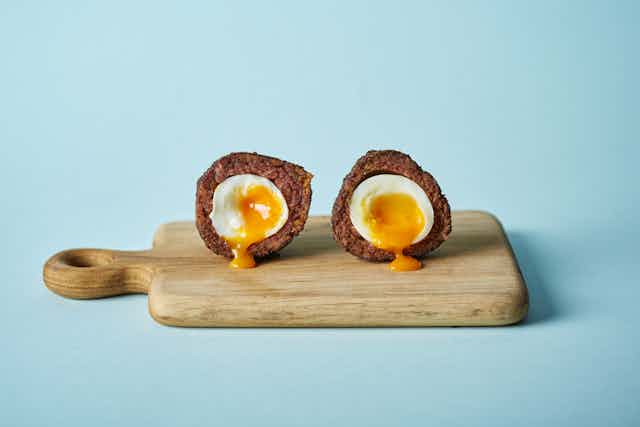 A scotch egg cut in two on a wooden board