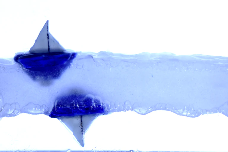 Small boats floating on and under a layer of levitating liquid.