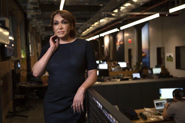 A transgender woman stands in business attire in an office