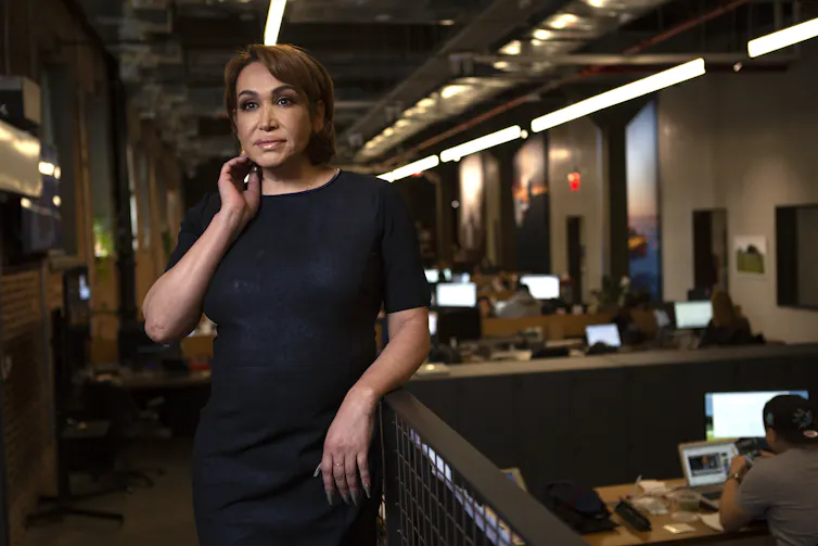 A transgender woman stands in business attire in an office