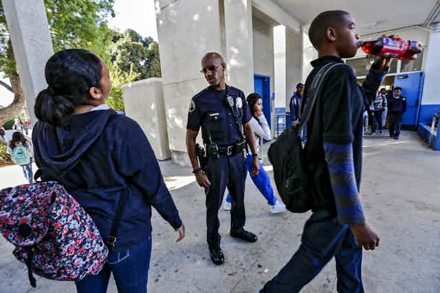An African American police officer looks at two African American students a school.