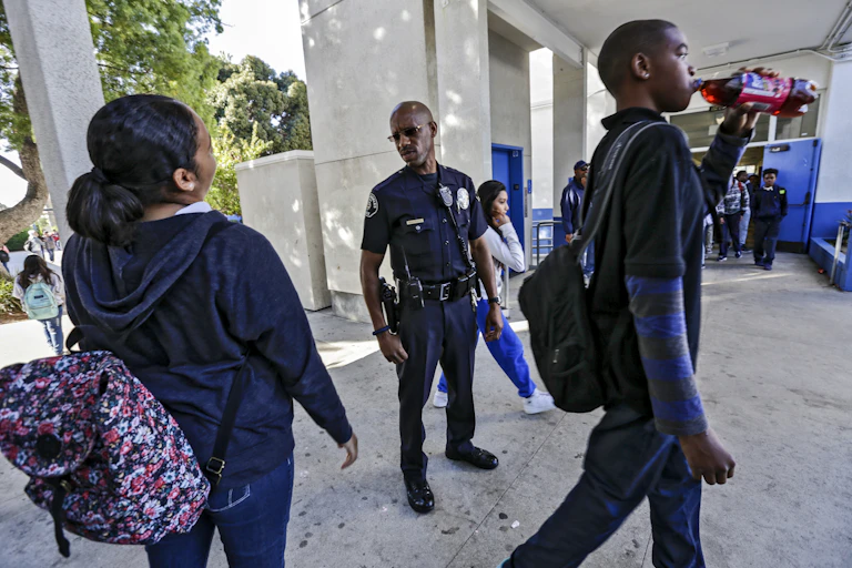 An African American police officer looks at two African American students a school.
