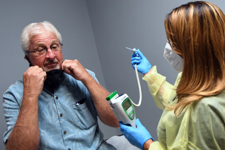 Tony Potts, a 69-year-old retiree, removes his face mask for a temperature check just before receiving his first injection in a Phase 3 COVID-19 vaccine clinical trial sponsored by Moderna.