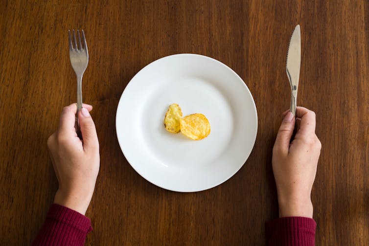 Two crisps sitting on a plate, about to be eaten with a knife and fork.