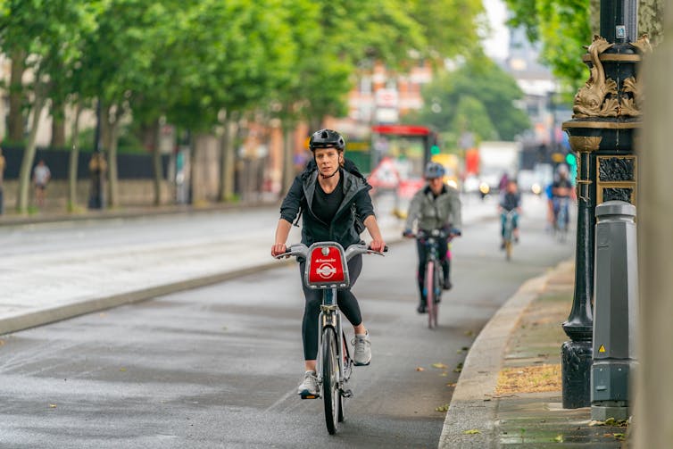 Cyclists riding down a tree-lined path in a city.