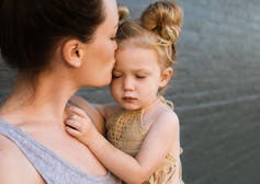 A woman cuddles a frowning little girl with side buns.