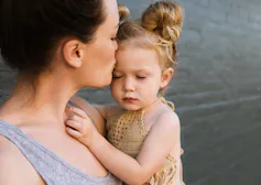 Une femme câline une petite fille qui fronce les sourcils avec des petits pains.