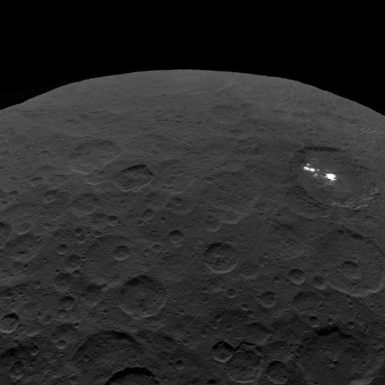 View of a dark asteroid in space showing two small bright spots.