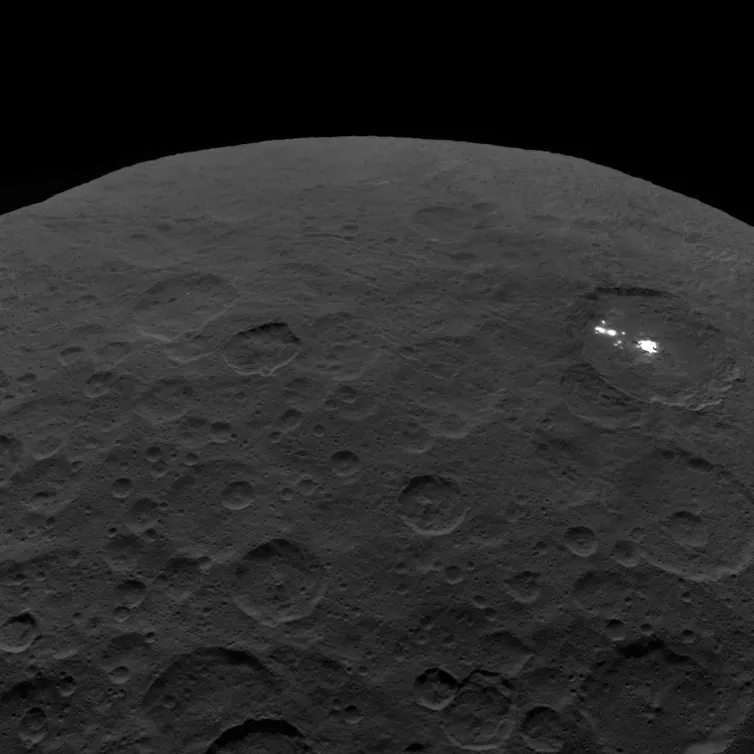 View of a dark asteroid in space showing two small bright spots.
