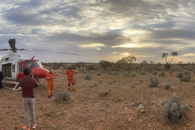 Several people and a helicopter in an outback Australian landscape.