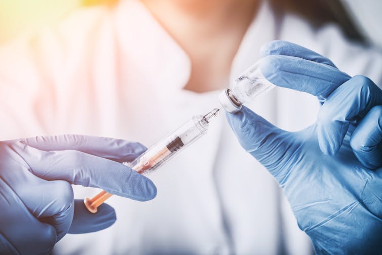 A doctor or scientists fills a syringe from a vaccine vial.