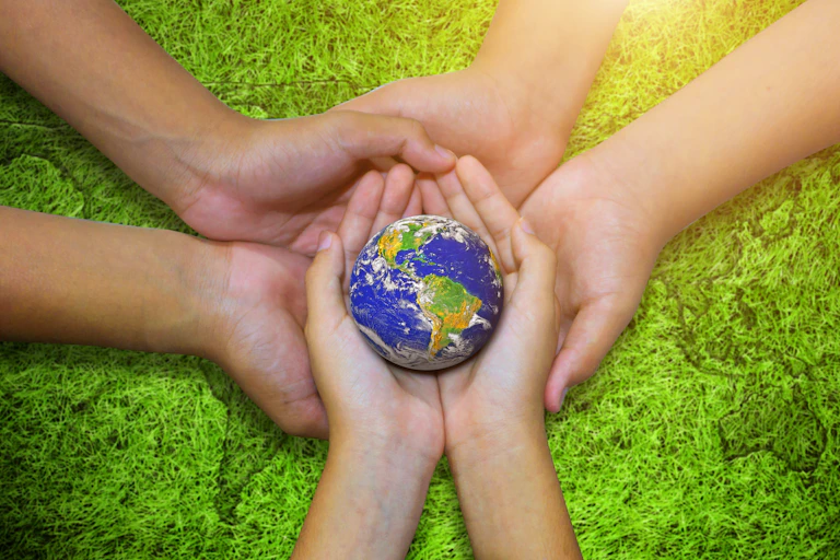 Three pairs of hands coming together to hold a small globe of the world