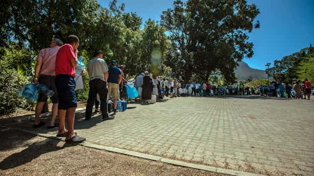 People queueing at a water point carrying water containers.
