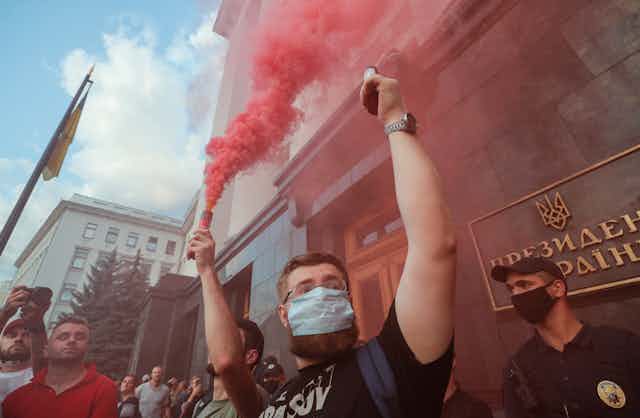 A man in a medical mask holds a red flare in protest at the ceasefire in eastern Ukraine.