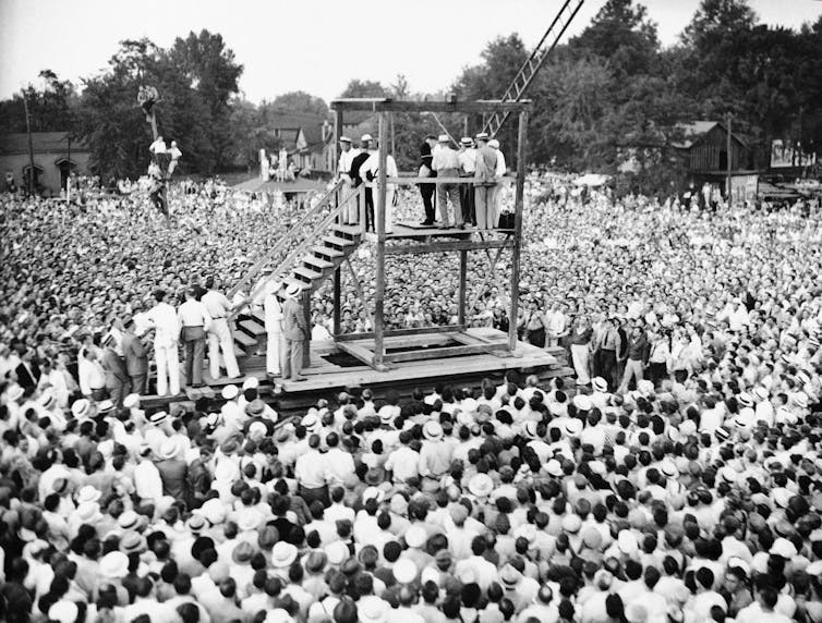 A wooden scaffold is surrounded by a crowd of people.