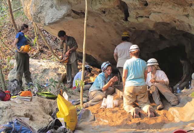 archaeologists excavate at the mouth of a cave