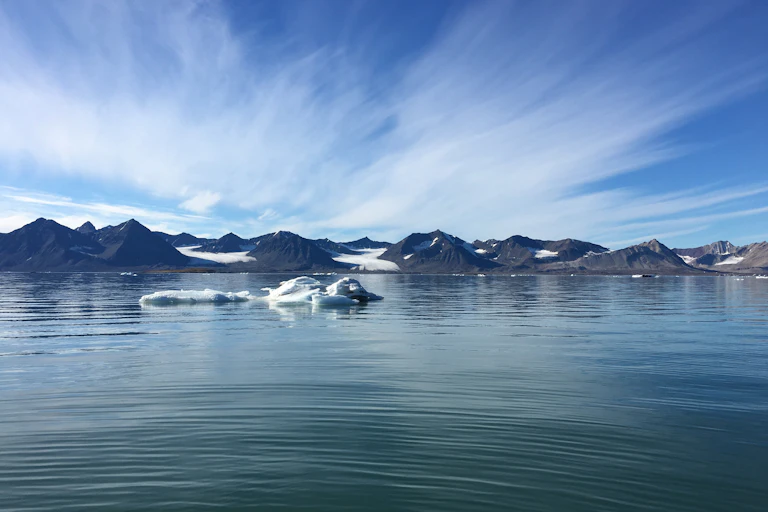 small iceberg in water with land peaks in background