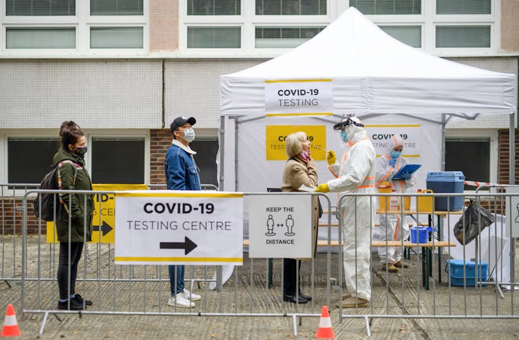 Three people queue outside a white gazebo to get a COVID-19 test.