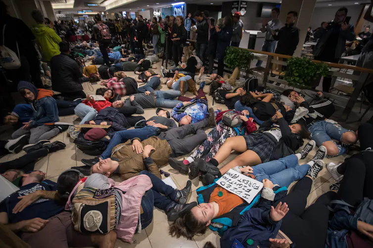 Dozens of young people lie on the floor of a food court.