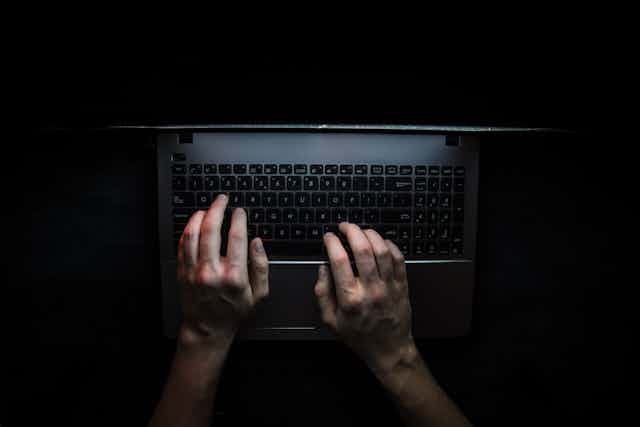 Two hands on a laptop keyboard, surrounded by darkness