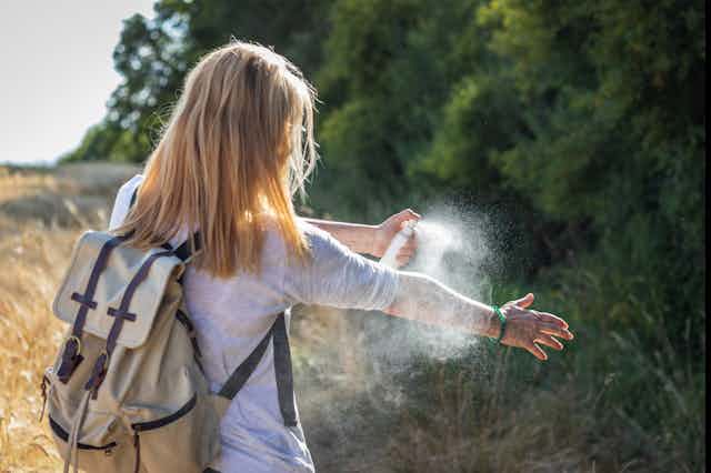 A woman applies insect repellent spray to her arm.