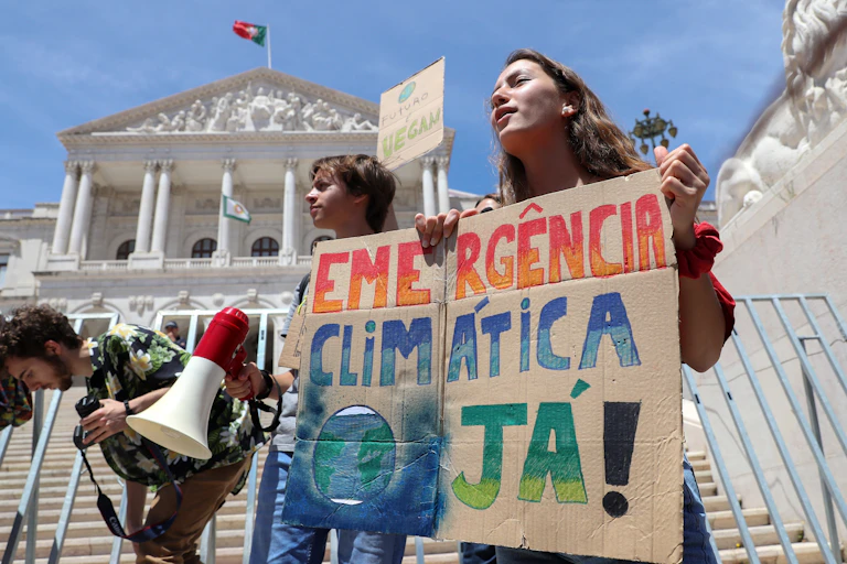 Children hold sign saying 'emercencia climatica ja!' in front of building flying a Portuguese flag