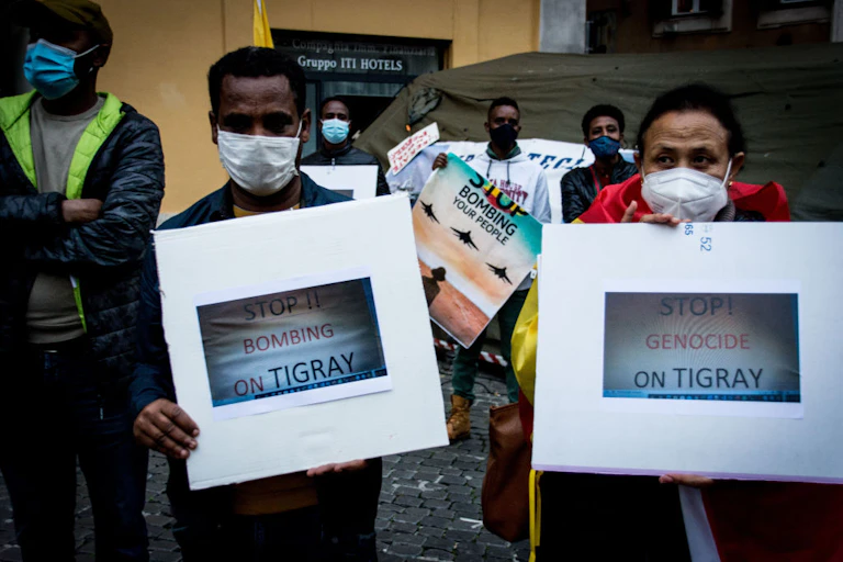 People stand outdoors wearing face masks and holding posters calling for an end to bombing an genocide in Tigray