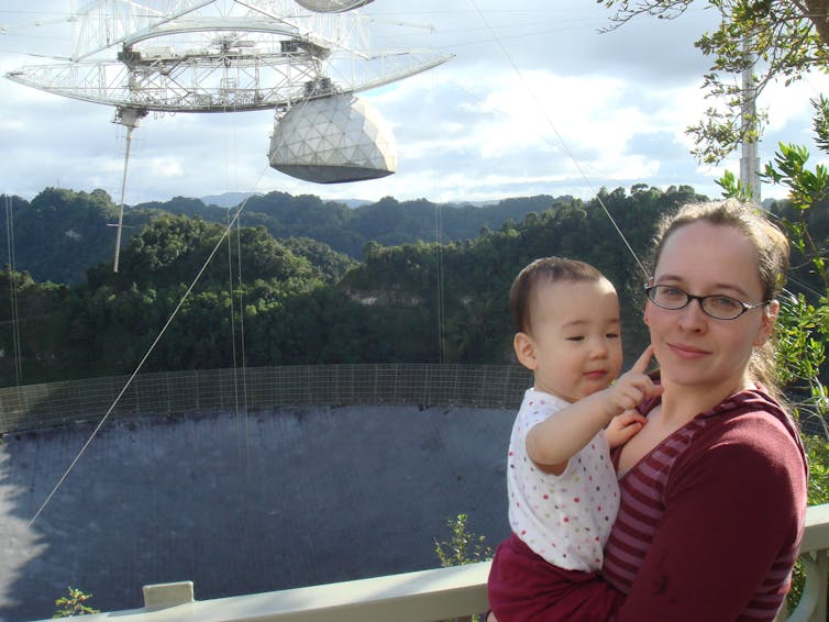 Woman and baby daughter stand in front of radio telescope.