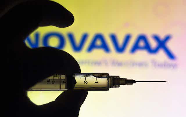 Hand holding a syringe with the company name Novovax in background