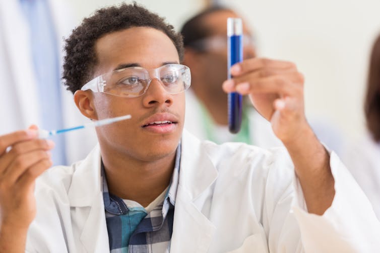 An African American male scientist is looking at a test tube in a lab.